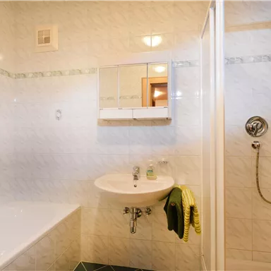 Ein modernes Badezimmer mit einer Badewanne, Dusche und Waschbecken. Die Wände sind hell gefliest und der Raum wirkt sauber und einladend.