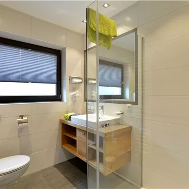 Ein modernes Badezimmer mit einer Duschkabine und einem Holzwaschbecken. Die hellen Fliesen und die grünen Handtücher sorgen für eine frische Atmosphäre.