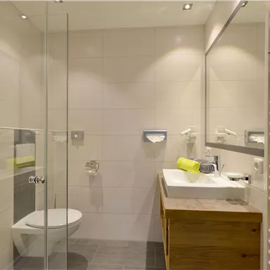 Ein modernes Badezimmer mit einer Glasdusche und einem Holzwaschtisch. Die Wände sind hell gefliest und mit Handtüchern in lebhaften Farben dekoriert.