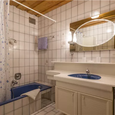 A bright bathroom with white tiles and a blue sink. There is a bathtub with a shower curtain and a large mirror.