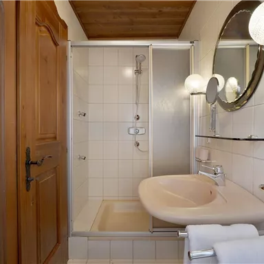 A modern bathroom with a shower, sink, and wood detailing. Bright tiles and a mirror create a friendly atmosphere.
