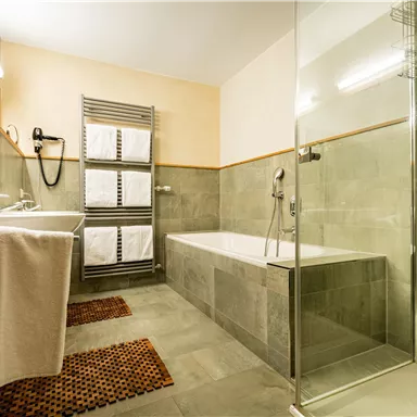 Ein modernes Badezimmer mit einer Badewanne und einer Dusche. Die Wände sind in neutralen Grautönen gehalten, und es gibt zwei Handtücher auf dem Waschbecken.