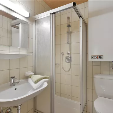 Ein modernes Badezimmer mit einer Dusche, einem Waschbecken und einer Toilette. Die Wände sind hell gefliest und es gibt ein großes Spiegel.