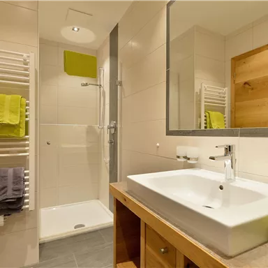 Ein modernes Badezimmer mit einer Dusche und einem Waschbecken. Handtücher in verschiedenen Farben sind ordentlich angeordnet.