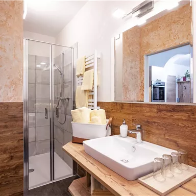 A modern bathroom with a glass shower and an elegant sink on a wooden shelf. The walls are painted in warm tones, creating an inviting atmosphere.