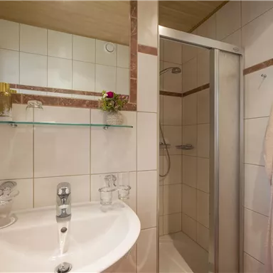A modern bathroom with a shower and a sink. The walls are tiled and a towel rack is visible.