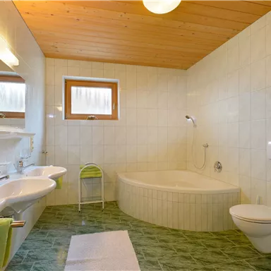 Ein modernes Badezimmer mit einer Badewanne und einem WC. Helle Fliesen und Holzdecken sorgen für eine freundliche Atmosphäre.