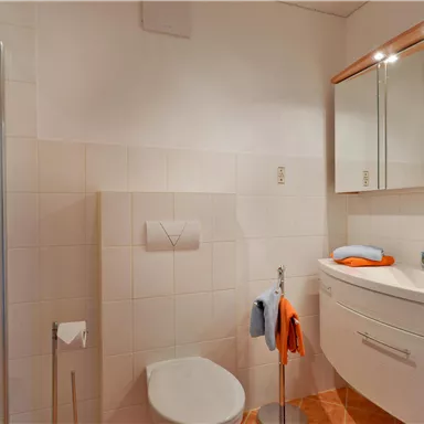 Ein modernes Badezimmer mit Dusche und einem Waschbecken. Es ist hell und gut gestaltet, mit weißen Fliesen und warmen Holztönen.