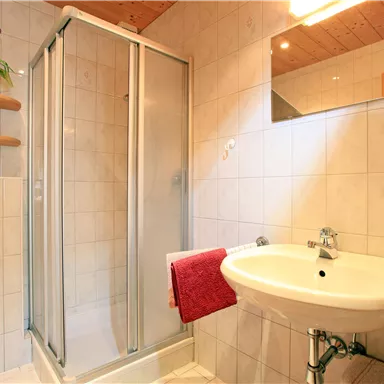 Ein kleines Badezimmer mit einer Duschkabine und einem Waschbecken. Die Wände sind gefliest und es gibt einen Handtuchhalter aus Holz.