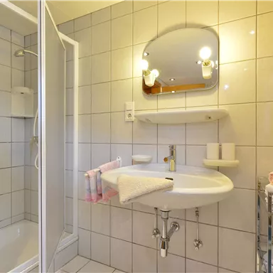Ein modernes Badezimmer mit einer Dusche und einem Waschbecken. Handtücher sind ordentlich auf einem Regal angeordnet.