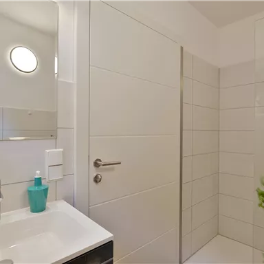 A modern bathroom with a shower and a sink. Bright tiles and a large wall mirror give the space an elegant look.