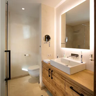 Ein modernes Badezimmer mit Holzschränken und einem eleganten Waschbecken. Die Dusche ist durch Glaswände abgetrennt, und es gibt eine große Spiegelwand.