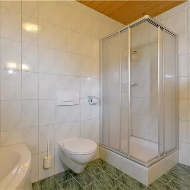 Ein helles Badezimmer mit einer Dusche und einer Badewanne. Die Wände sind gefliest und der Boden hat einen grünen Belag.