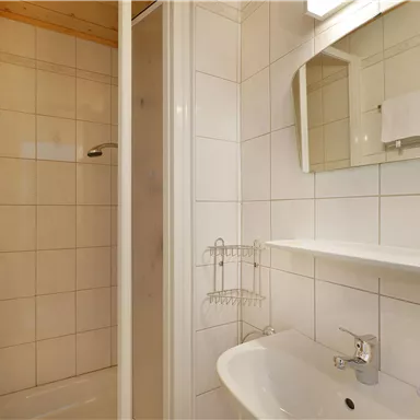 A small bathroom with a shower and a sink. The walls are tiled and there are towels as well as a mirror.