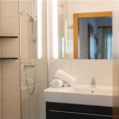 A modern bathroom with a glass shower and a large mirror. There are towels on the sink and bright walls.