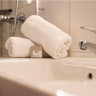 A modern bathroom with a sink and fresh, white towels. Next to the towels lies a bar of soap.