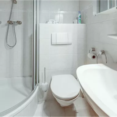 A modern bathroom with a shower cabin and a bathtub. The walls are tiled in light colors and personal care products are visible.