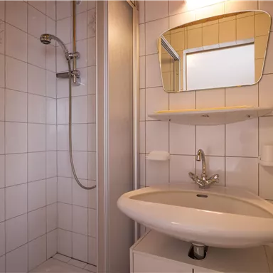 A modern bathroom with a shower and a sink. The walls are tiled, and a mirror hangs above the sink.
