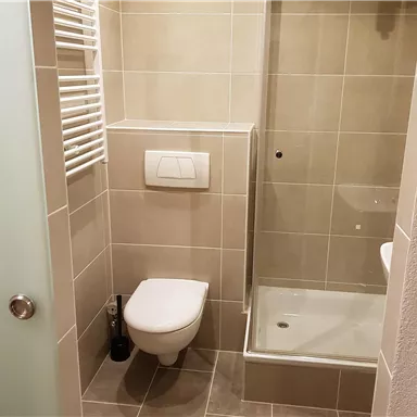 A modern bathroom with a shower and a toilet. The walls are tiled in neutral tones and there is a towel warmer.