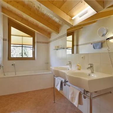 Ein modernes Badezimmer mit einer Badewanne und zwei Waschbecken. Große Fenster sorgen für viel Tageslicht.