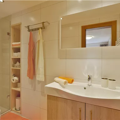 A modern bathroom with a shower and a sink. There are wooden shelves and useful accessories in neutral colors.
