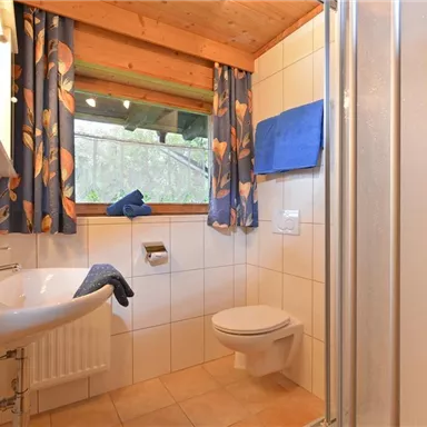A modern bathroom with a shower and a sink. The windows let in a lot of light, and the colorful curtains give the room a fresh atmosphere.