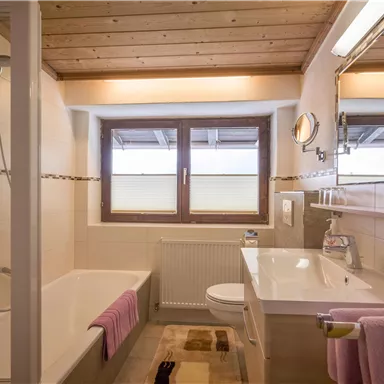 A modern bathroom with a bathtub and a shower. The decor is bright and inviting, featuring a wooden ceiling and large windows.