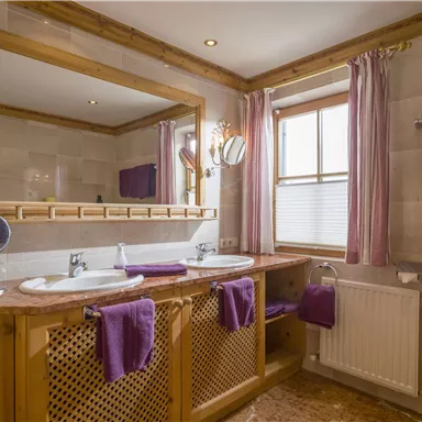 A modern bathroom with two sinks and large mirrors. The walls are light and decorated with purple towels.