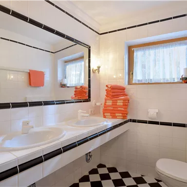 A modern bathroom with two sinks and large mirrors. Clean, stacked towels in bright orange add a fresh accent to the space.