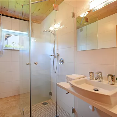 Ein modernes Badezimmer mit einer Glasdusche und einem hellen Waschbecken. Der Raum ist gut beleuchtet und hat eine freundliche Atmosphäre.