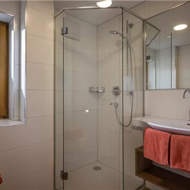 Ein modernes Badezimmer mit einer gläsernen Dusche und einem Waschtisch. Die Handtücher sind in leuchtendem Orange gehalten.