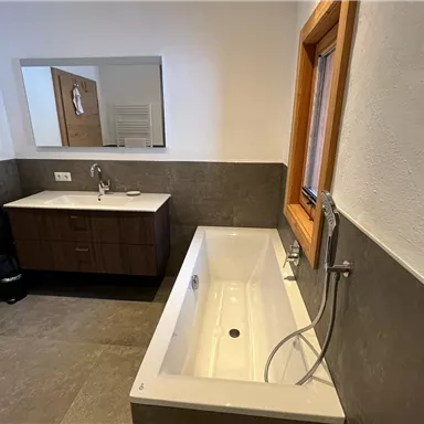 Ein modernes Badezimmer mit einer freistehenden Badewanne und einem stilvollen Waschbecken. Die Wände sind in neutralen Farben gehalten, und ein Fenster sorgt für natürliches Licht.