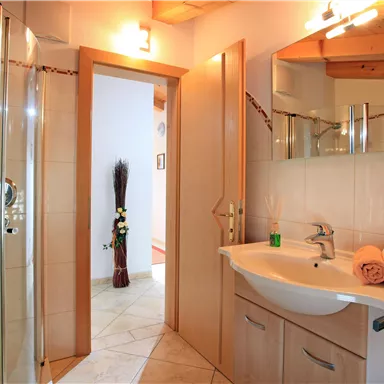 A modern bathroom with a shower and a sink. Towels are placed on the table, and the room is brightly lit.