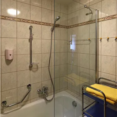 Ein modernes Badezimmer mit einer Badewanne und einer Duschabtrennung aus Glas. Handtücher und ein Regal mit Pflegeartikeln sind ebenfalls vorhanden.