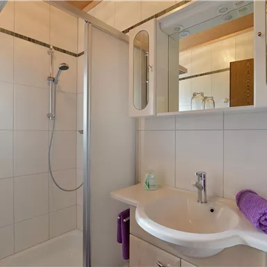 A modern bathroom with a shower and a sink. Towels and toiletries are neatly arranged.