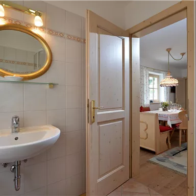 A modern bathroom with a round mirror and a sink. In the background, a cozy living area is visible.