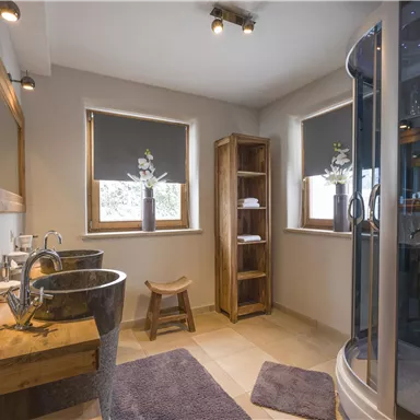 Ein modernes Badezimmer mit Holz- und Glasakzenten. Der Raum ist hell und einladend, mit einer Dusche und stilvollen Waschbecken.