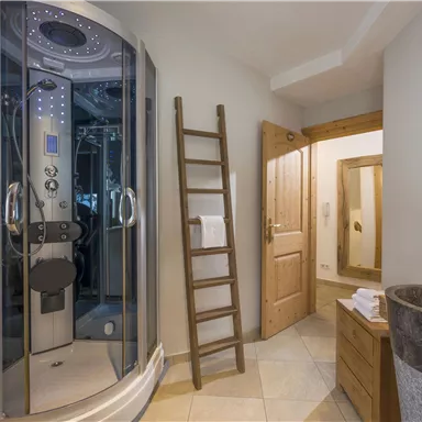 Ein modernes Badezimmer mit einer massiven Dusche und eleganten Holzdetails. Eine Holzleiter und ein stilvolles Waschbecken runden das Ambiente ab.