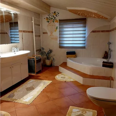 A bright bathroom with modern tiles and a bathtub. The decor is simple and inviting, with plants and decorative mats.