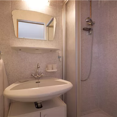 A small bathroom with a shower and vanity. The walls are light tiled and equipped with a mirror.