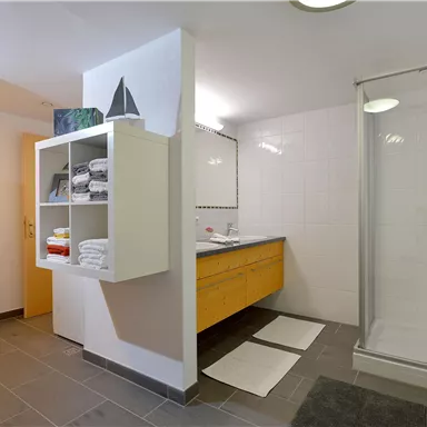 Ein modernes Badezimmer mit einer Dusche und einem großen Spiegel. Im Hintergrund sind Handtücher und Pflanzen dekorativ angeordnet.