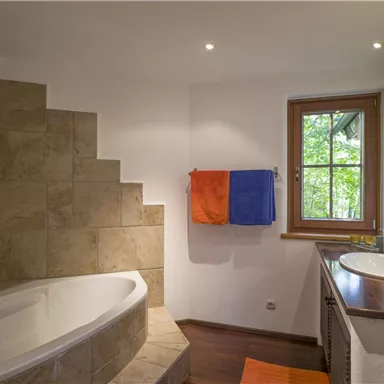 A modern bathroom with a bathtub and a shower. Colorful towels hang on the wall and a window provides daylight.