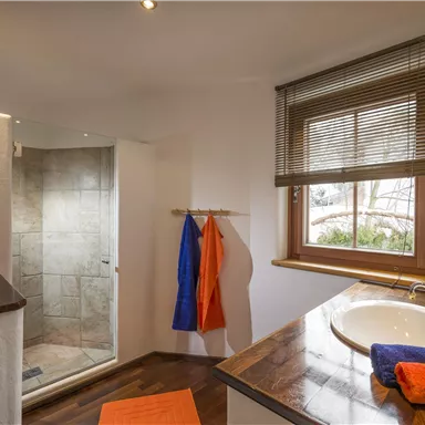 A bright bathroom with a shower and a sink. Colorful towels hang on the wall and a window provides natural light.