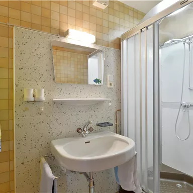 Ein kleines Badezimmer mit einer Dusche, einem Waschbecken und einem Spiegel. Die Wände sind mit hellen Fliesen in einem minimalistischen Design verkleidet.