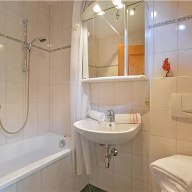 Ein modernes Badezimmer mit einer Badewanne, einem Waschbecken und einem Spiegel. Die Wände sind gefliest, und es gibt saubere Handtücher.