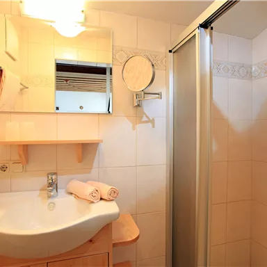A modern bathroom with a shower cabin and a wooden sink. Two towels and toiletries are placed beside it.
