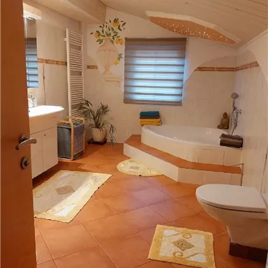 A modern bathroom with a bathtub and a sink. The space is bright and friendly with decorative elements and terracotta flooring.