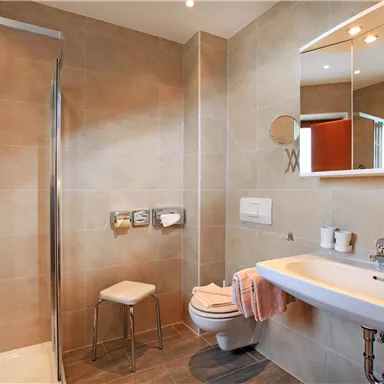 Ein modernes Badezimmer mit einer Dusche, einem Waschbecken und einem WC. Die Wände sind in dezenten Farbtönen gehalten und es gibt sanitäre Einrichtungen wie Handtücher und Pflegeprodukte.