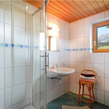 Ein helles Badezimmer mit einer Dusche, einem Waschbecken und einem Fenster. Der Holzdecken und die Fliesen schaffen eine angenehme Atmosphäre.