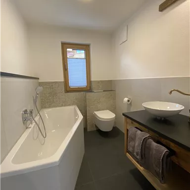 A modern bathroom with a bathtub and a sink. The walls are painted in a neutral tone and there is a window for natural light.